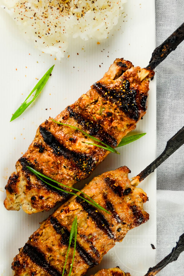 Grilled chicken tsukune (meatballs) on bamboo skewers, served with green onions and rice topped with seaweed and sesame seeds