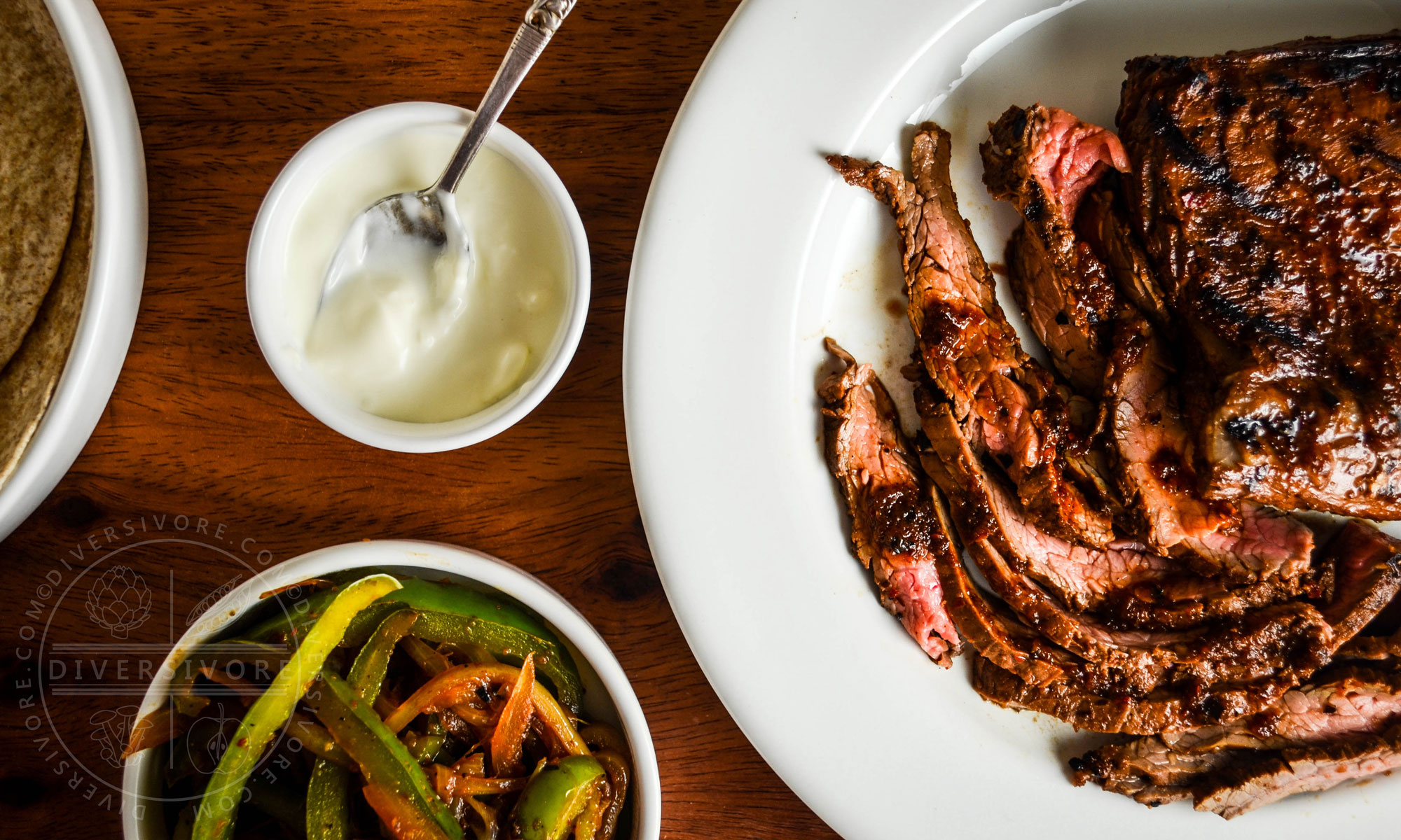 Carne Asada Borracha on a white plate with Mexican crema and cooked peppers & onions