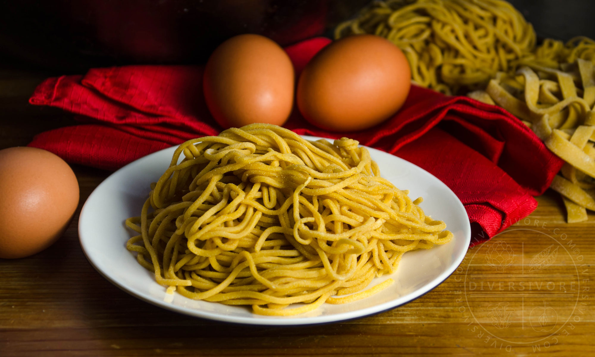Homemade Chinese egg noodles on a white plate, in front of a red cloth and brown eggs.