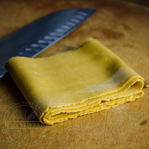 A sheet of egg noodles, uncut, shown with a santoku knife.