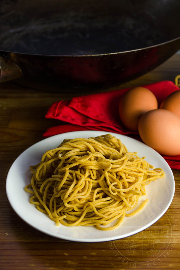 Homemade Chinese egg noodles on a white plate, in front of a red cloth and brown eggs.