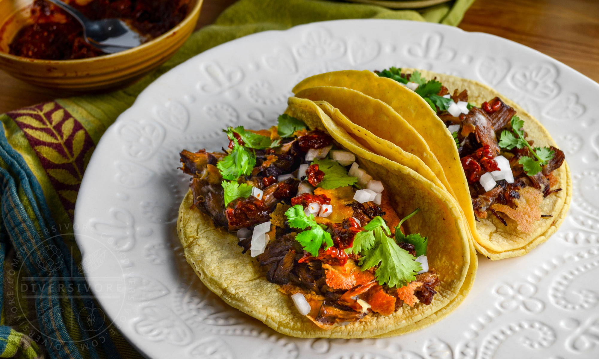 Pressure cooker Carnitas con Queso (tender beef bites with crispy melted cheese) served in corn tortillas on a textured white plate