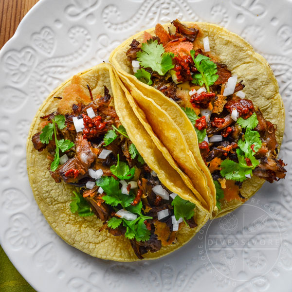 Instant Pot Carnitas con Queso served in corn tortillas with onions and spicy dried chili salsa