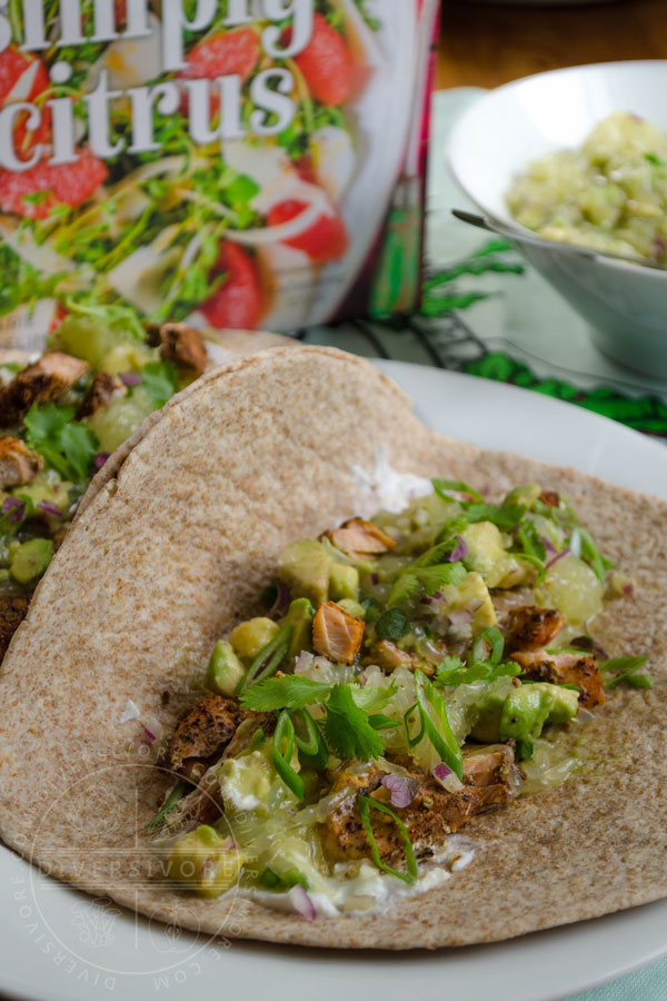 Broiled fish tacos with avocado-grapefruit salsa served in a whole wheat tortilla on a white plate, flanked by a copy of Simply Citrus by Marie Asselin