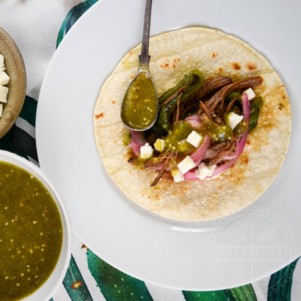 Instant Pot Brisket with Pasilla-Morita Adobo, served in a taco with salsa verde, pickled onions, and queso fresco