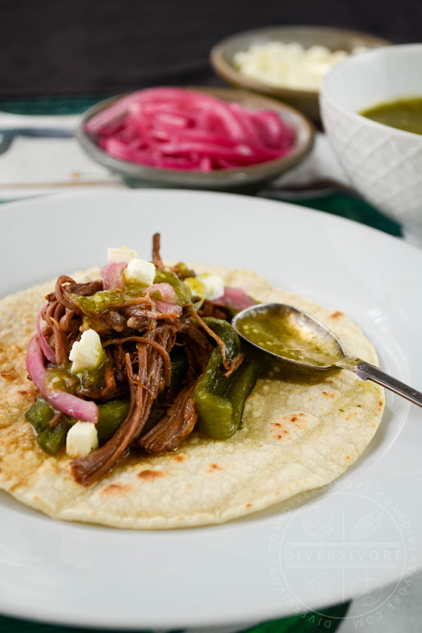 Instant Pot Brisket with Pasilla-Morita Adobo, served in a taco with salsa verde, pickled onions, and queso fresco