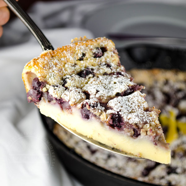 A slice of Saskatoon berry clafoutis being lifted from a skillet with a cake server