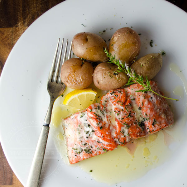 Simple herbed salmon with lemon garlic butter, served with potatoes and a sprig of savory