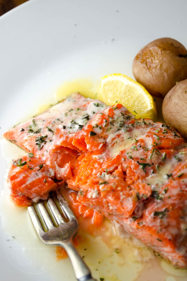 A fork taking a piece out of a salmon fillet topped with lemon garlic butter