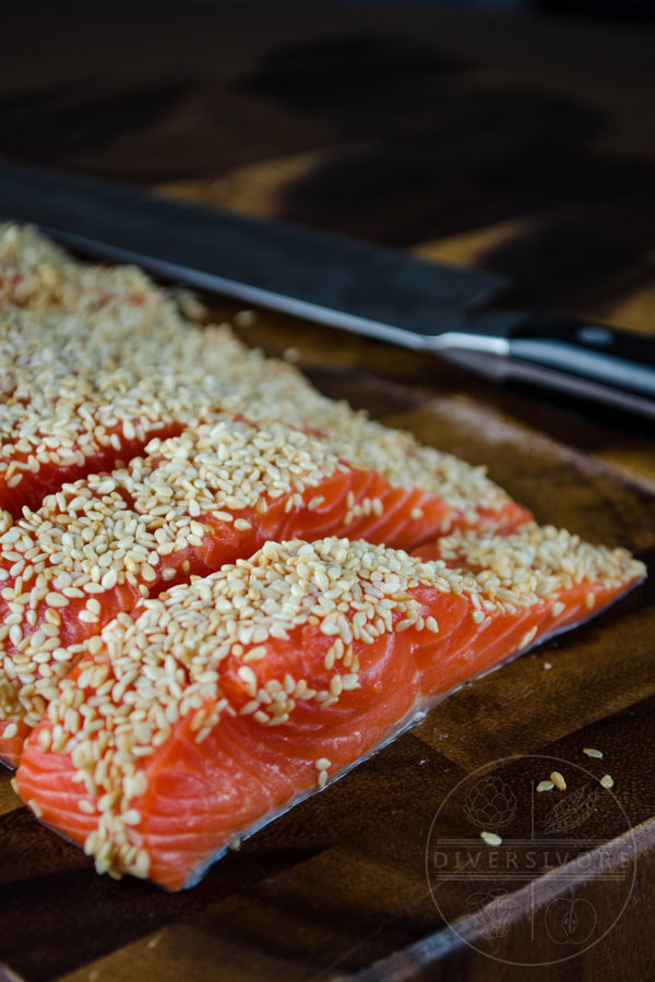Salmon fillets covered in sesame seeds, shown on a walnut board
