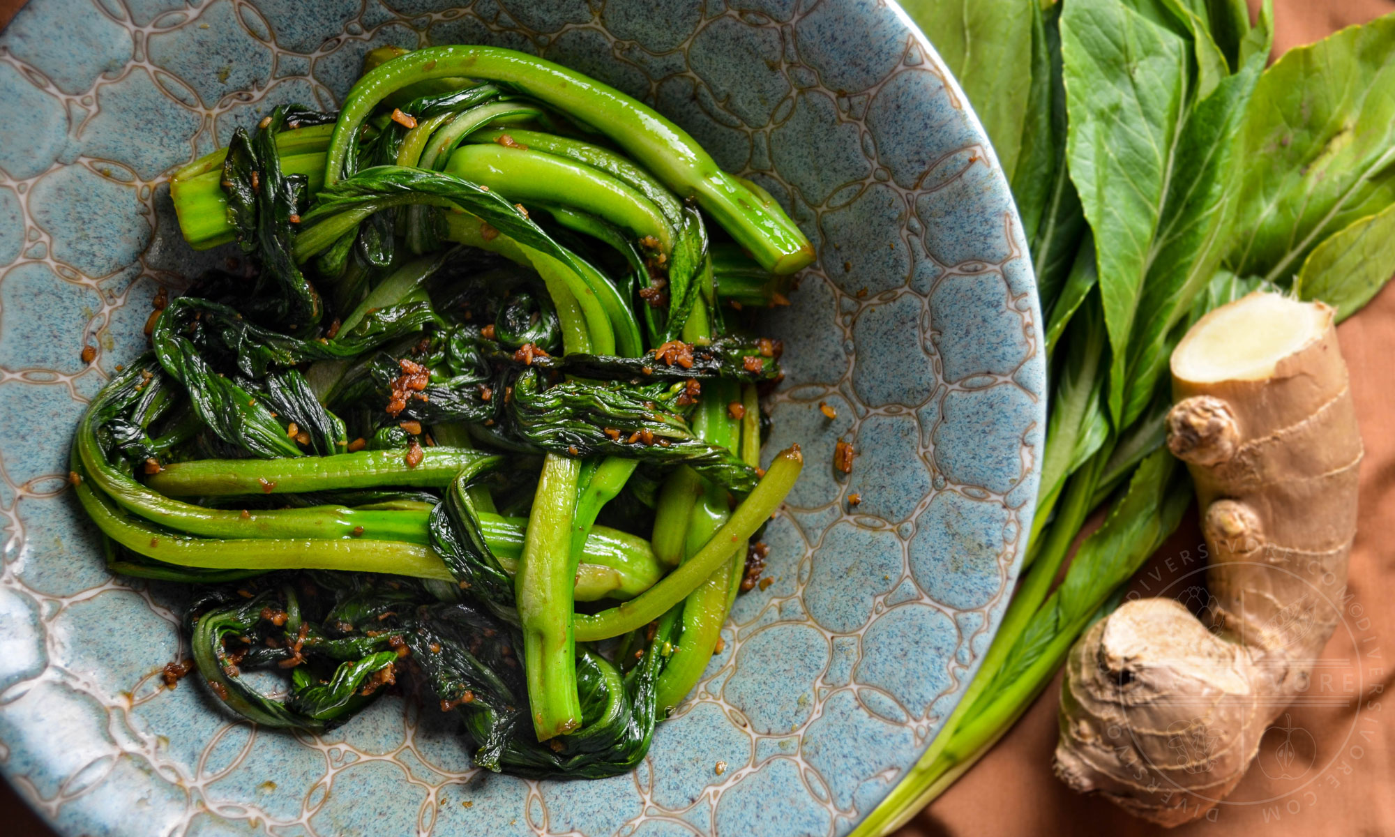 Stir-fried choy sum in a decorative ceramic bowl beside a knob of ginger