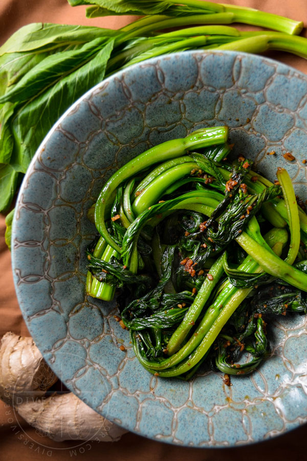 Stir-fried choy sum in a decorative ceramic bowl beside a knob of ginger