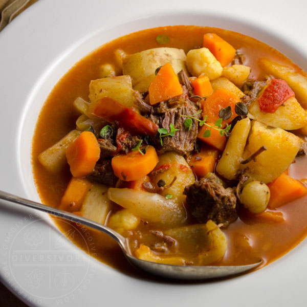 Beef cheek gulyasleves (goulash soup) with vegetables and a spoon in a white bowl