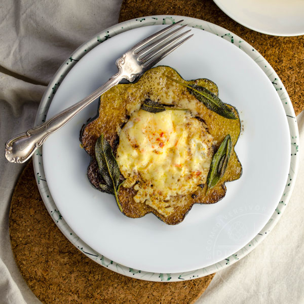 Squash Hole-in-One (aka Egg in a basket, aka Toad in the hole) made with eggs, acorn squash, aged cheddar, and fried sage, shown on a white plate with a fork
