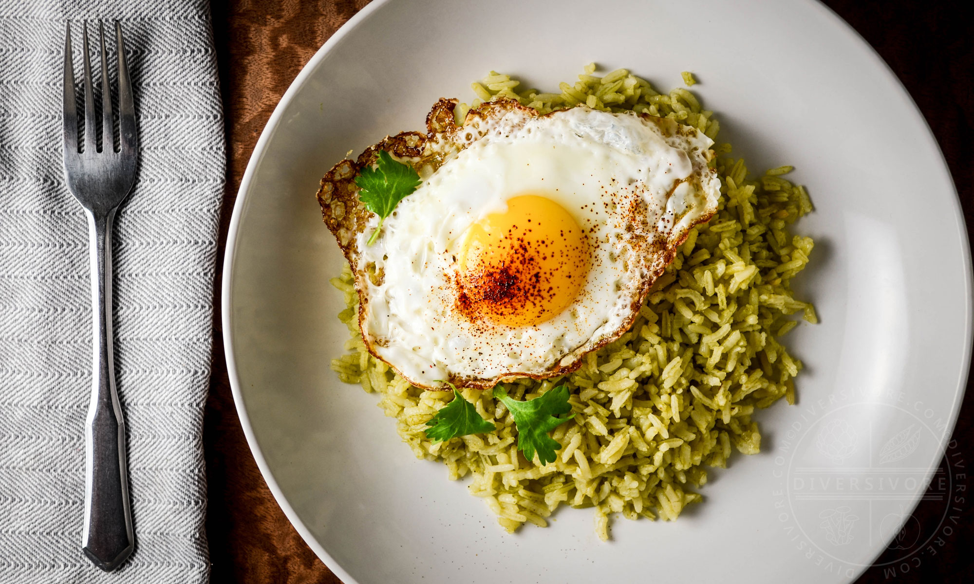 Green Rice (Arroz Verde) on a large white plate, topped with a fried egg dusted with ancho chili powder.