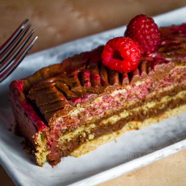 Chocolate Raspberry Rose Icebox Cake slice topped with two raspberries and served on a rectangular plate