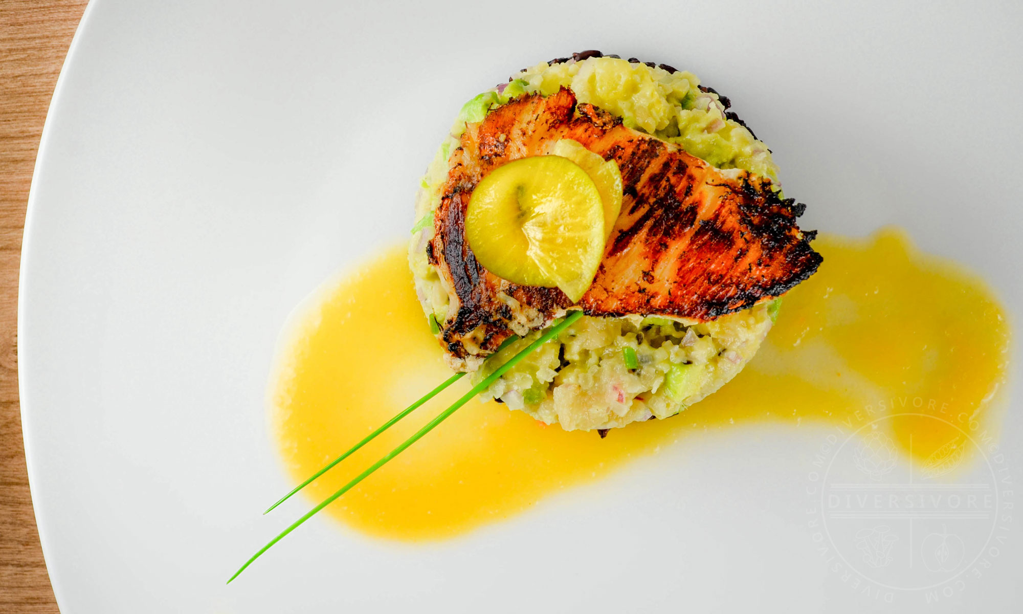 Seared Halibut cheeks with avocado-kiwi-macadamia tartare on forbidden rice, garnished with golden kiwi sauce and chives