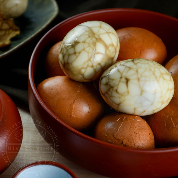 Taiwanese tea eggs, both peeled and unpeeled, in a bowl beside a clay tea pot