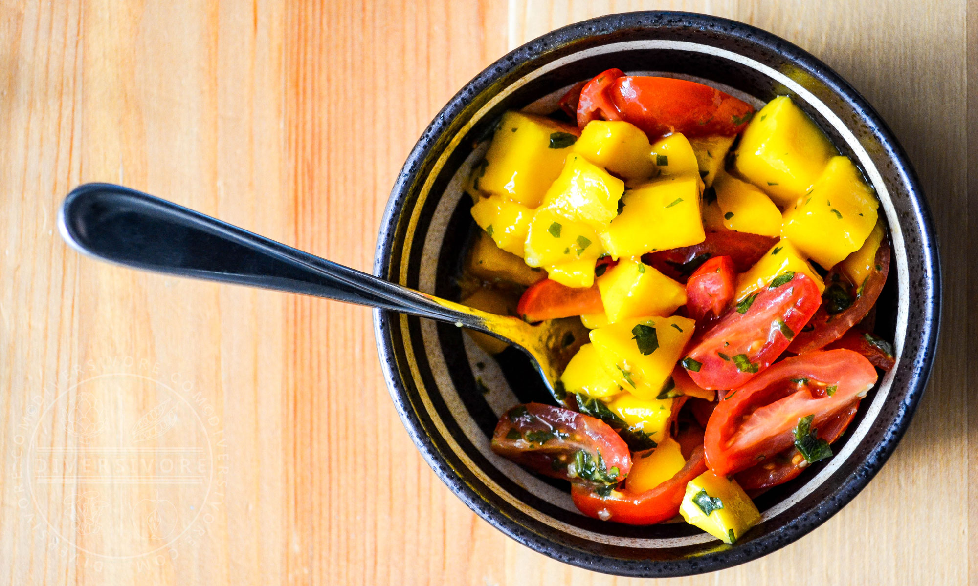 Mango and tomato salad with mint chimichurri in a bowl with a spoon