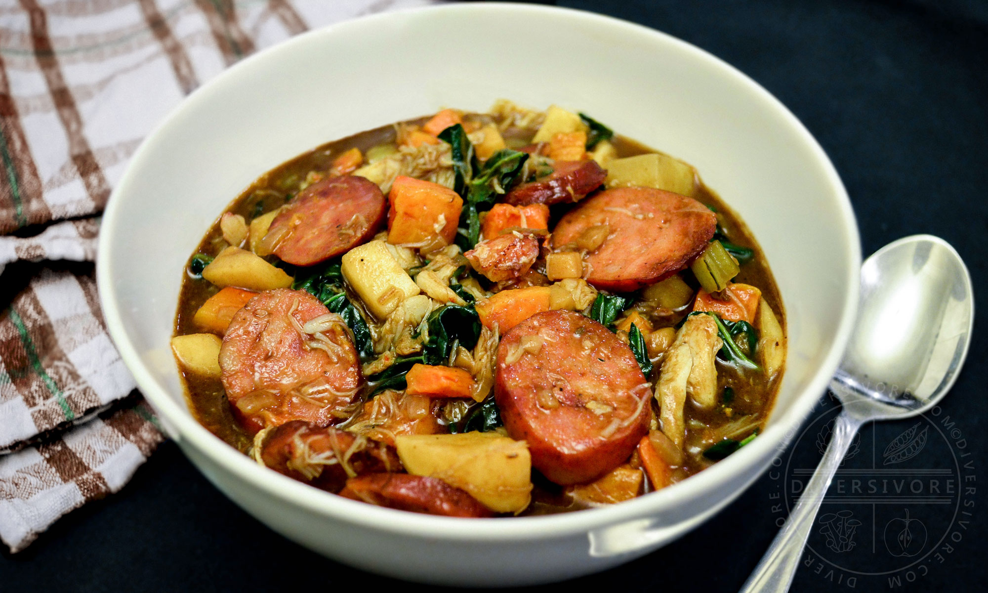 A bowl of winter gumbo made with Pacific Northwest ingredients, served beside a brown and white plaid towel and a spoon