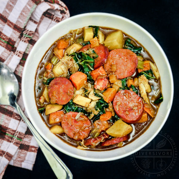 Winter gumbo with andouille sausage, crab, and various vegetables next to a checkered cloth and a spoon