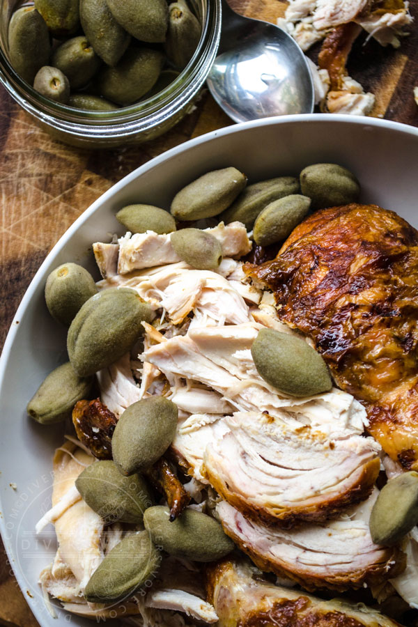 Pickled green almonds with roast chicken in a large white bowl