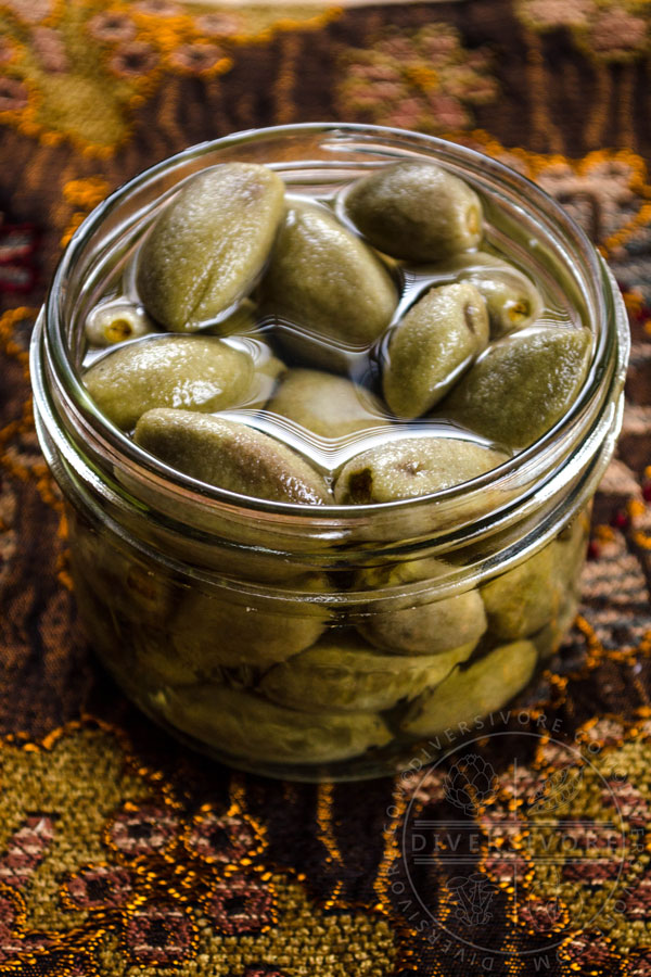 Pickled green almonds in a glass jar filled with brine on a patterned cloth