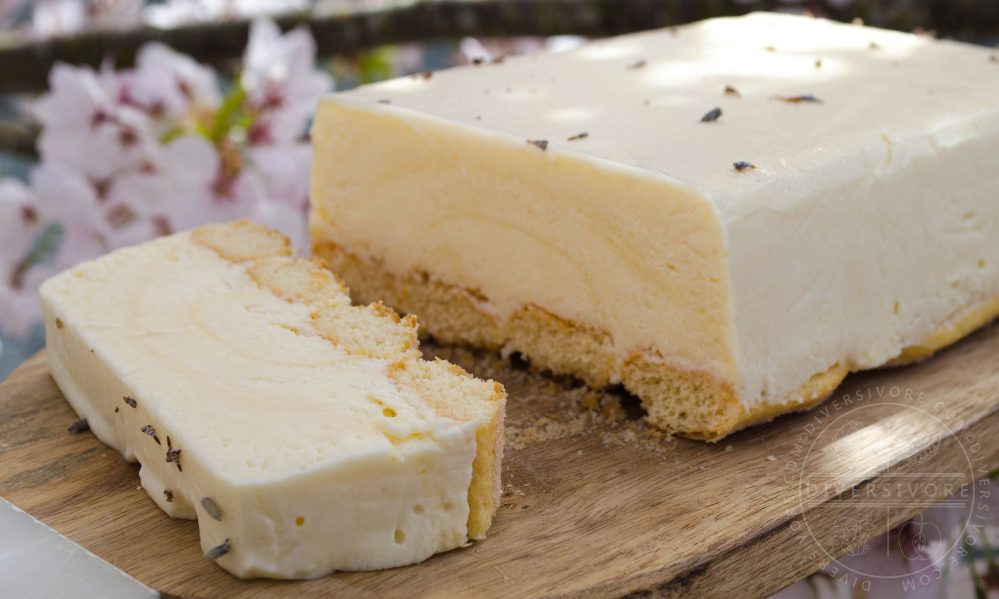 Easy Lemon and Lavender Semifreddo with one slice cut off, shown on a wood board against a backdrop of cherry flowers