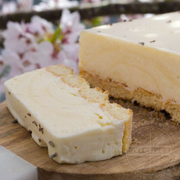 Easy Lemon and Lavender Semifreddo with one slice cut off, shown on a wood board against a backdrop of cherry flowers