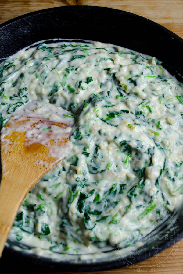 Creamed spinach and artichokes in a cast iron pan, being stirred with a wooden spoon