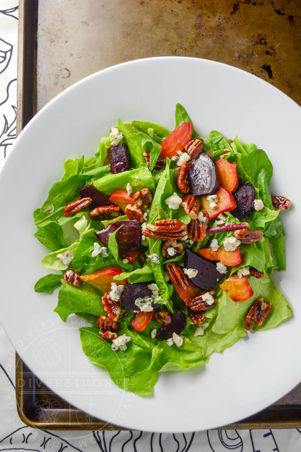 Dandelion and butterleaf lettuce salad with roasted beets, blue cheese, and maple-candied pecans in a white bowl against an old baking tray