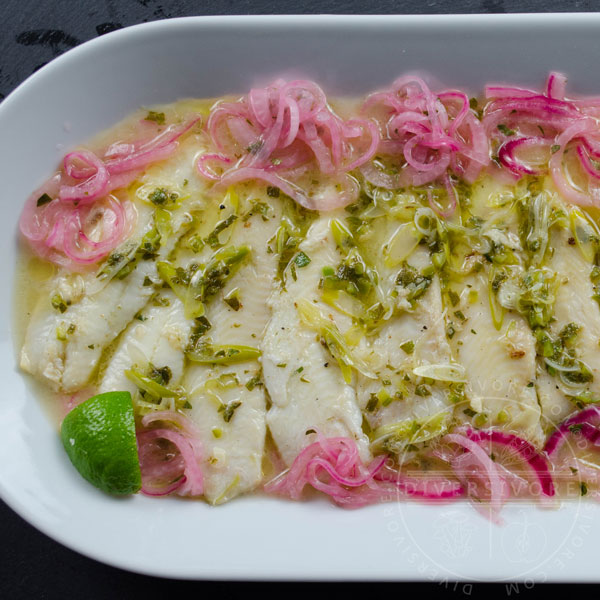 Pescado con vino - fish with white wine, cooked in a Mexican style, served in tacos with wine-pickled onions served in a shallow white platter with a wedge of lime