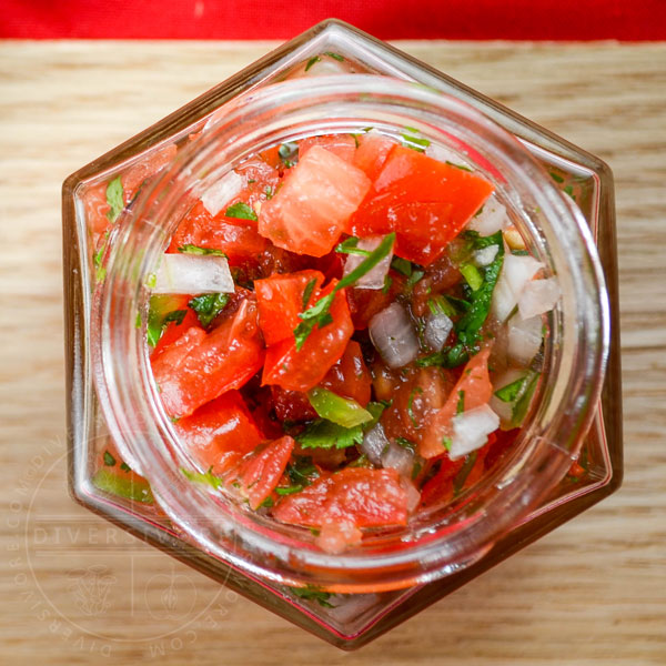 Pico de Gallo in a small hexagonal glass jar against a wood backdrop