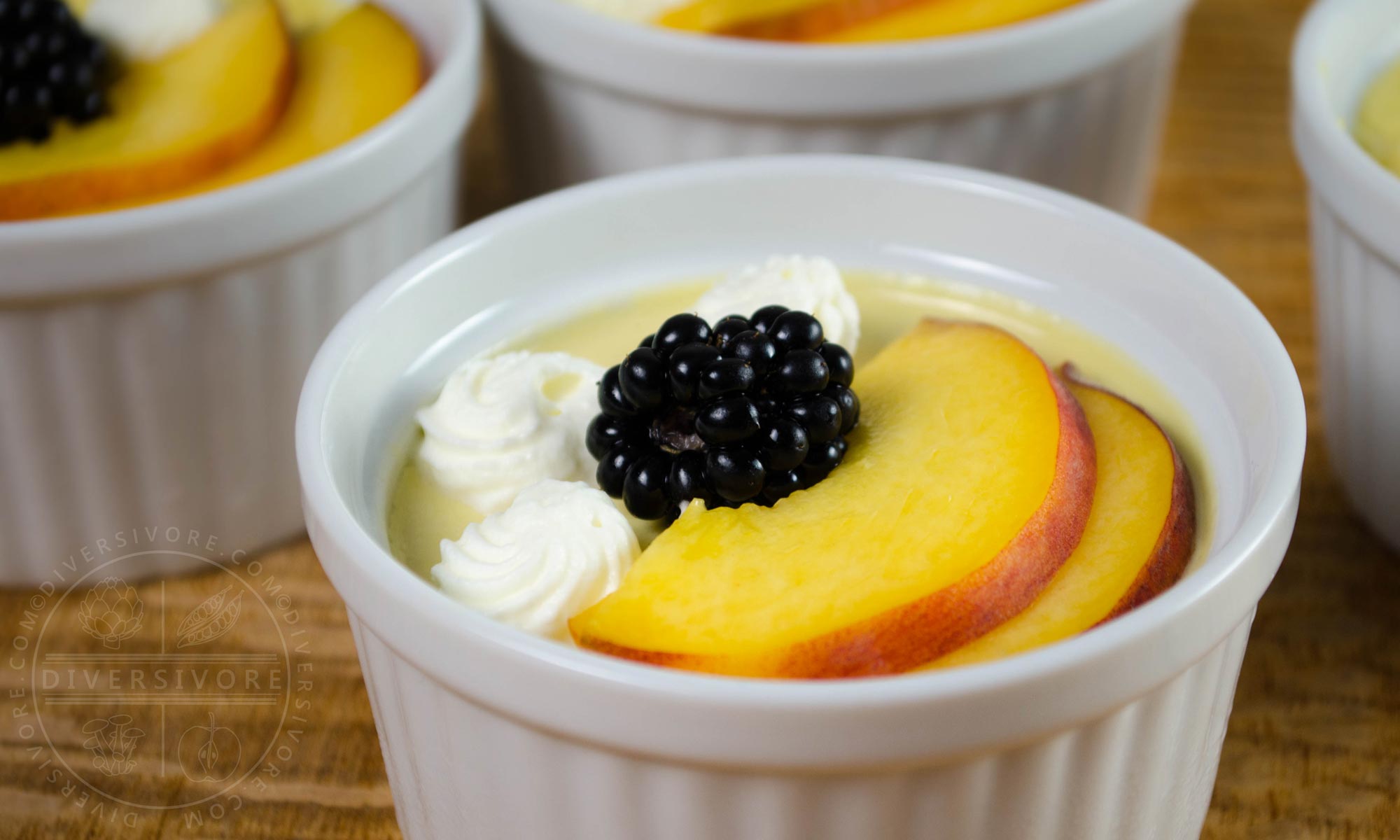 Peach pots de creme with peach slices and a blackberry in a white ramekin, flanked by additional ramekins