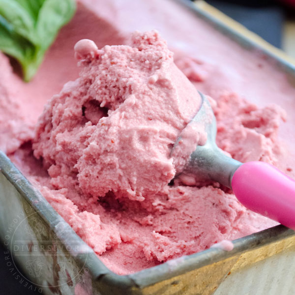 A scoop being taken out of a container of strawberry, basil, and goat cheese ice cream, decorated with basil leaves