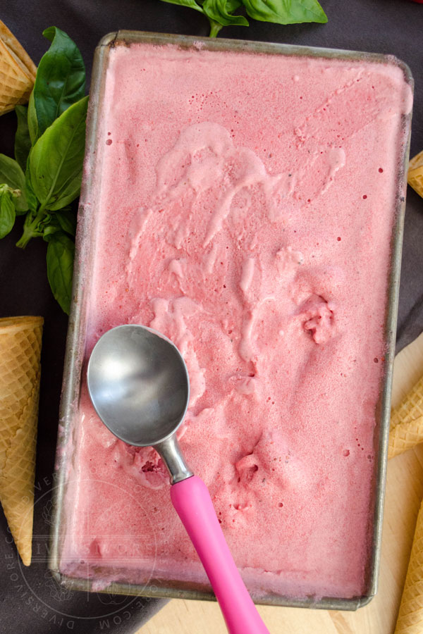 A container of strawberry, basil, and goat cheese ice cream, with a pink-handled ice cream scoop