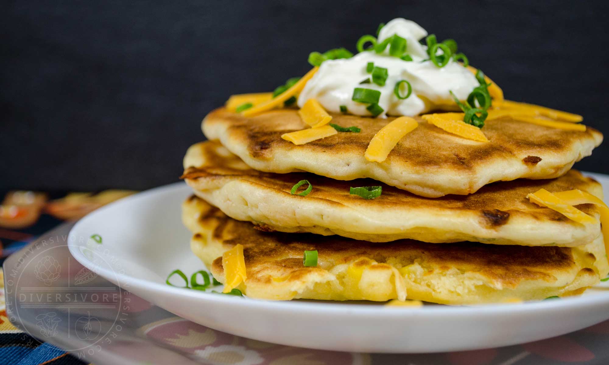 Bacon, cheddar, and chive pancakes topped with sour cream, cheese, and chives, all served on a white plate