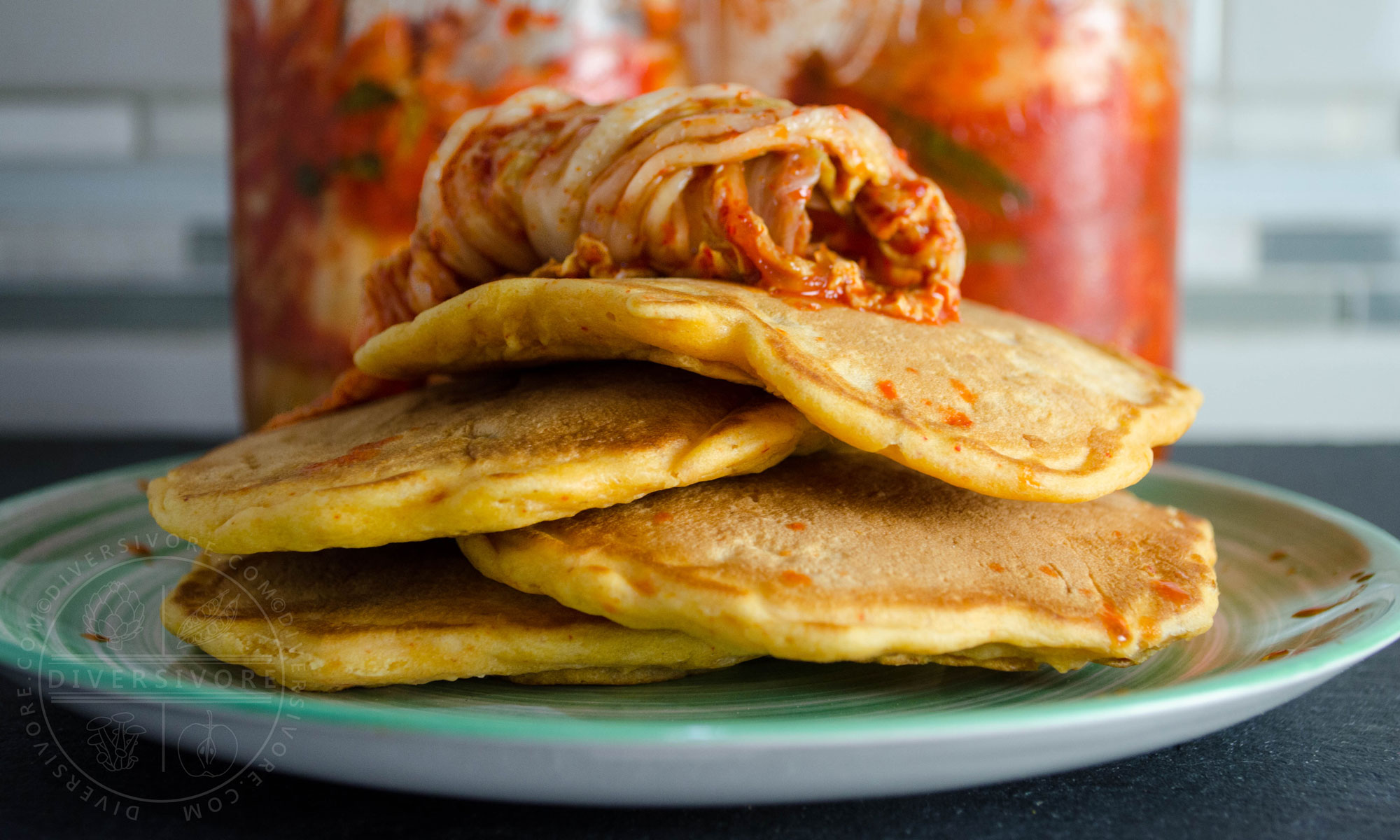 Kimchi and seafood pancakes on a green plate, topped with kimchi