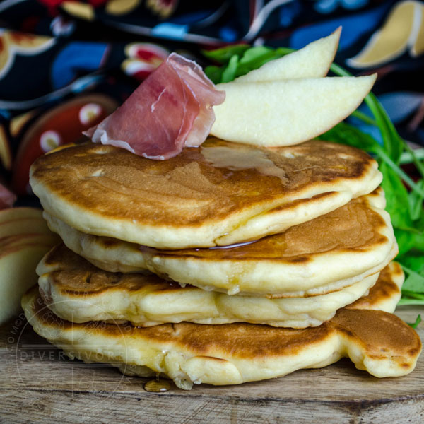 Pancakes with prosciutto, apple, and arugula on a wooden board.