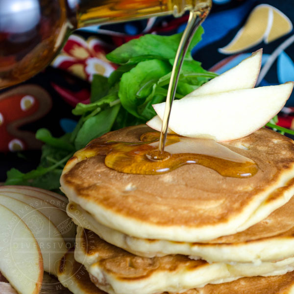 Maple syrup being poured on a stack of prosciutto, apple, and arugula pancakes