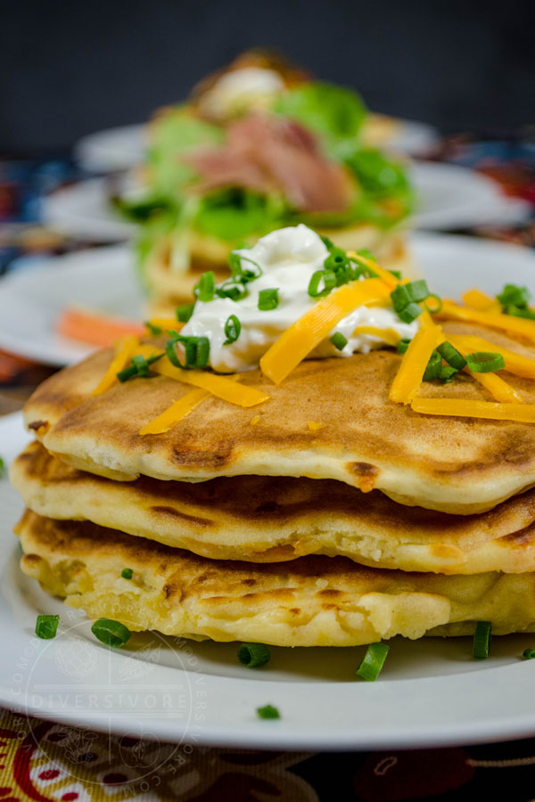 Bacon, cheddar, and chive pancakes topped with sour cream, cheese, and chives in front of several other savory pancake varieties.