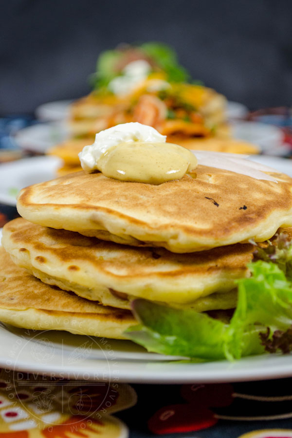 Savory pancakes with corn and kielbasa topped with mustard and sour cream in front of other savory pancake variations.