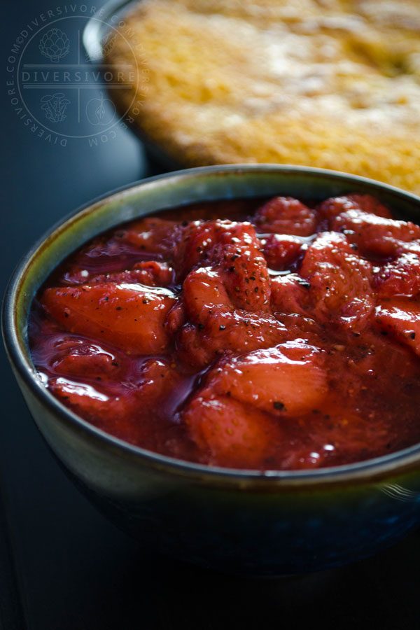 Strawberry and black pepper compote in a dark blue bowl, in front of a strawberry polenta cake