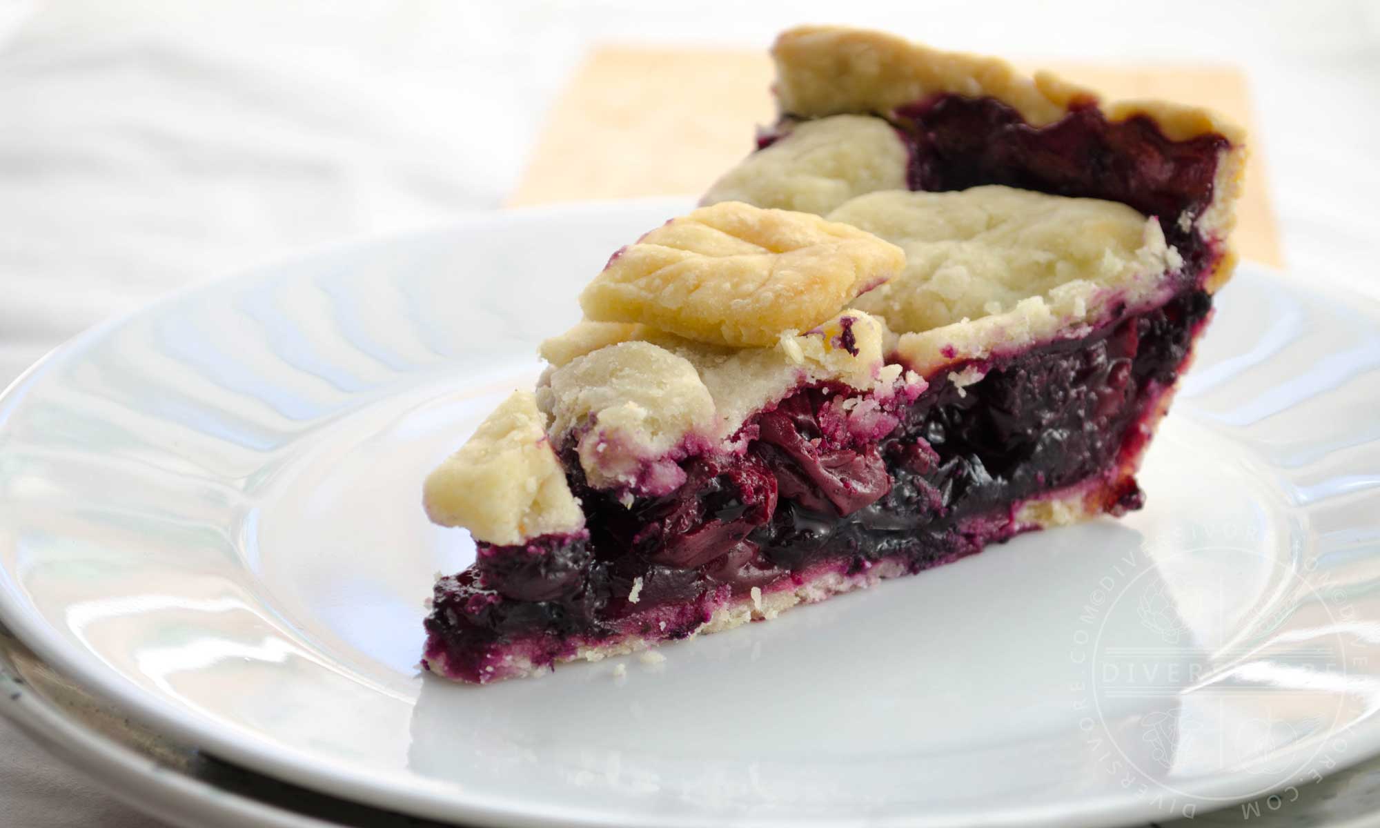 A slice of cherry-blueberry pie on a white plate