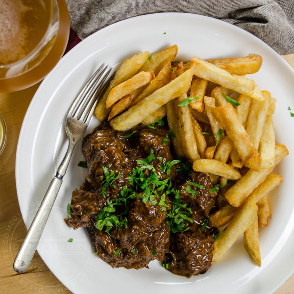 Carbonnade - Flemish Beef and Beer Stew in a white bowl with fries, a silver fork, and a glass of beer