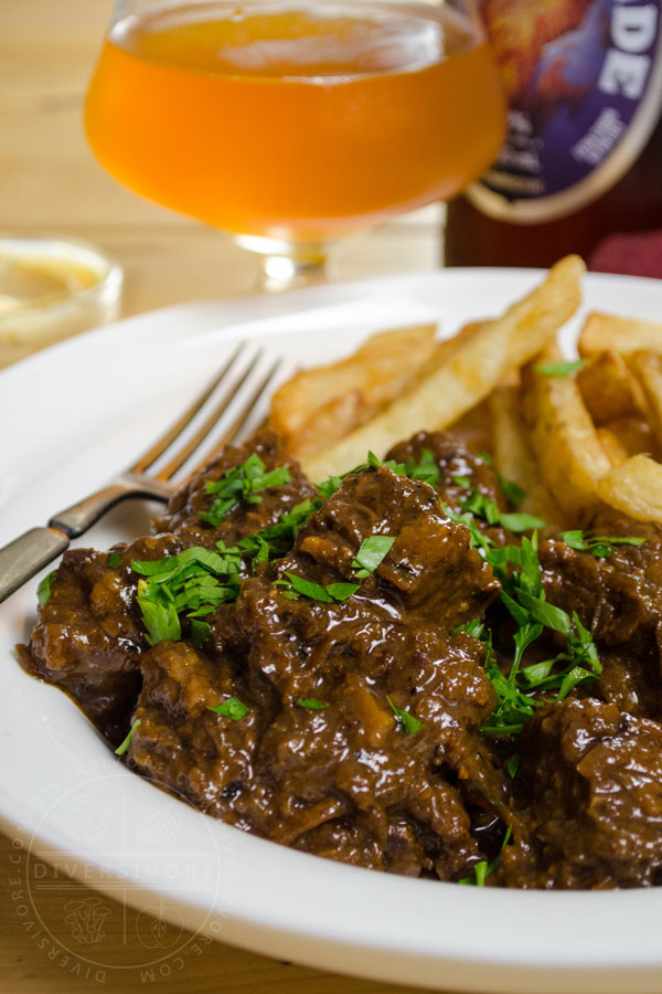 Carbonnade - Flemish Beef and Beer Stew in a white bowl with fries, a silver fork, and a glass of beer