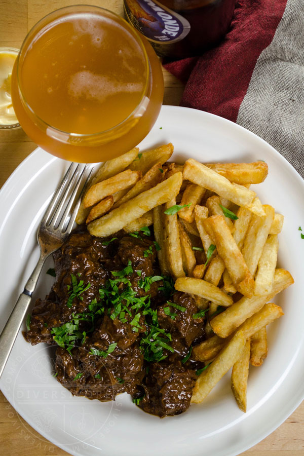 Carbonnade - Flemish Beef and Beer Stew in a white bowl with fries, a silver fork, and a glass of beer