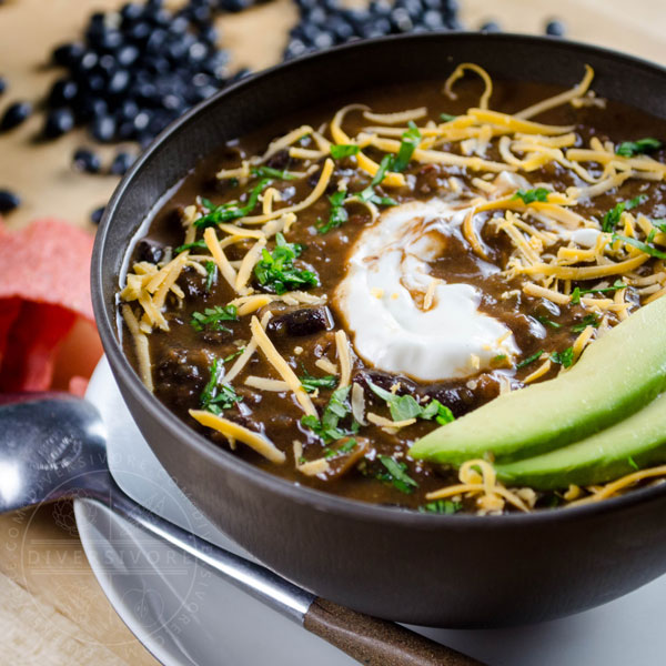 A bowl of Chili Mole with avocado, sour cream, and shredded cheese