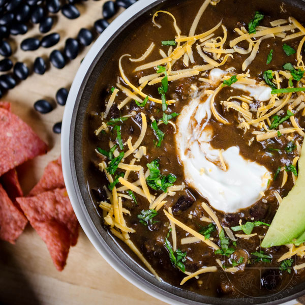 A bowl of Chili Mole with avocado, sour cream, and shredded cheese