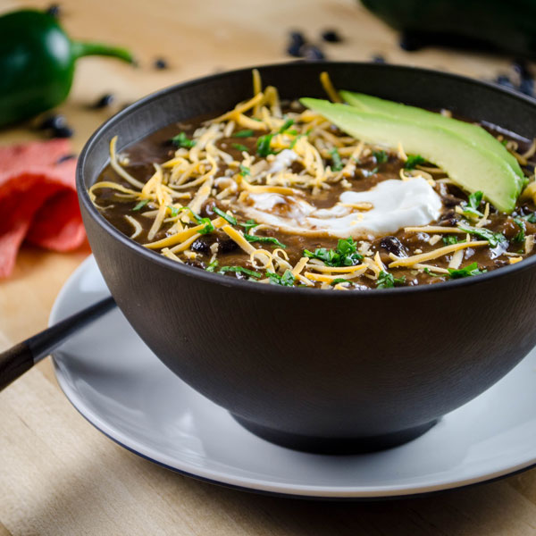 A bowl of Chili Mole with avocado, sour cream, and shredded cheese